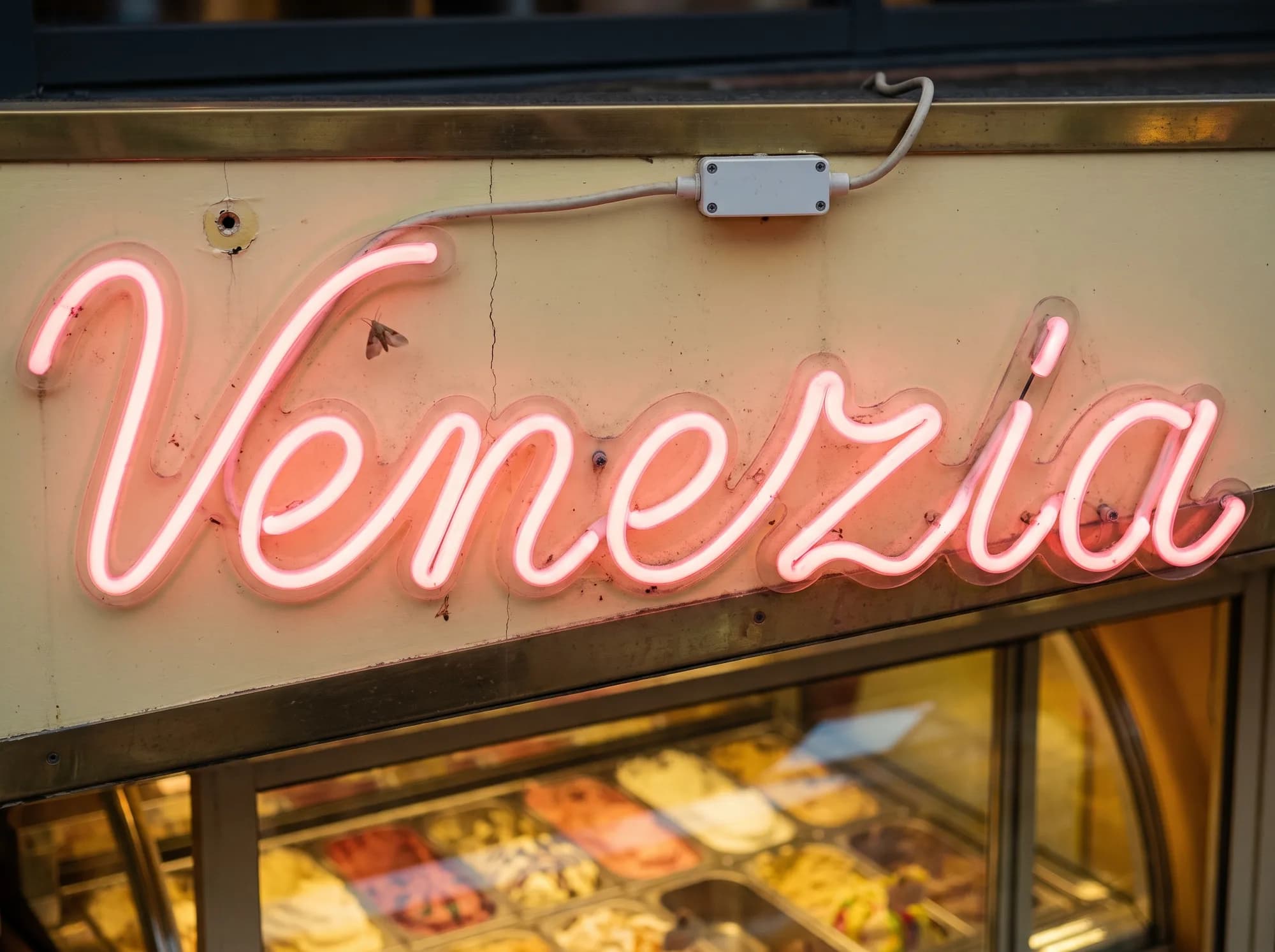 Rosafarbener Neon-Schriftzug in Schreibschrift auf der cremefarbenen Blende einer Eisdiele