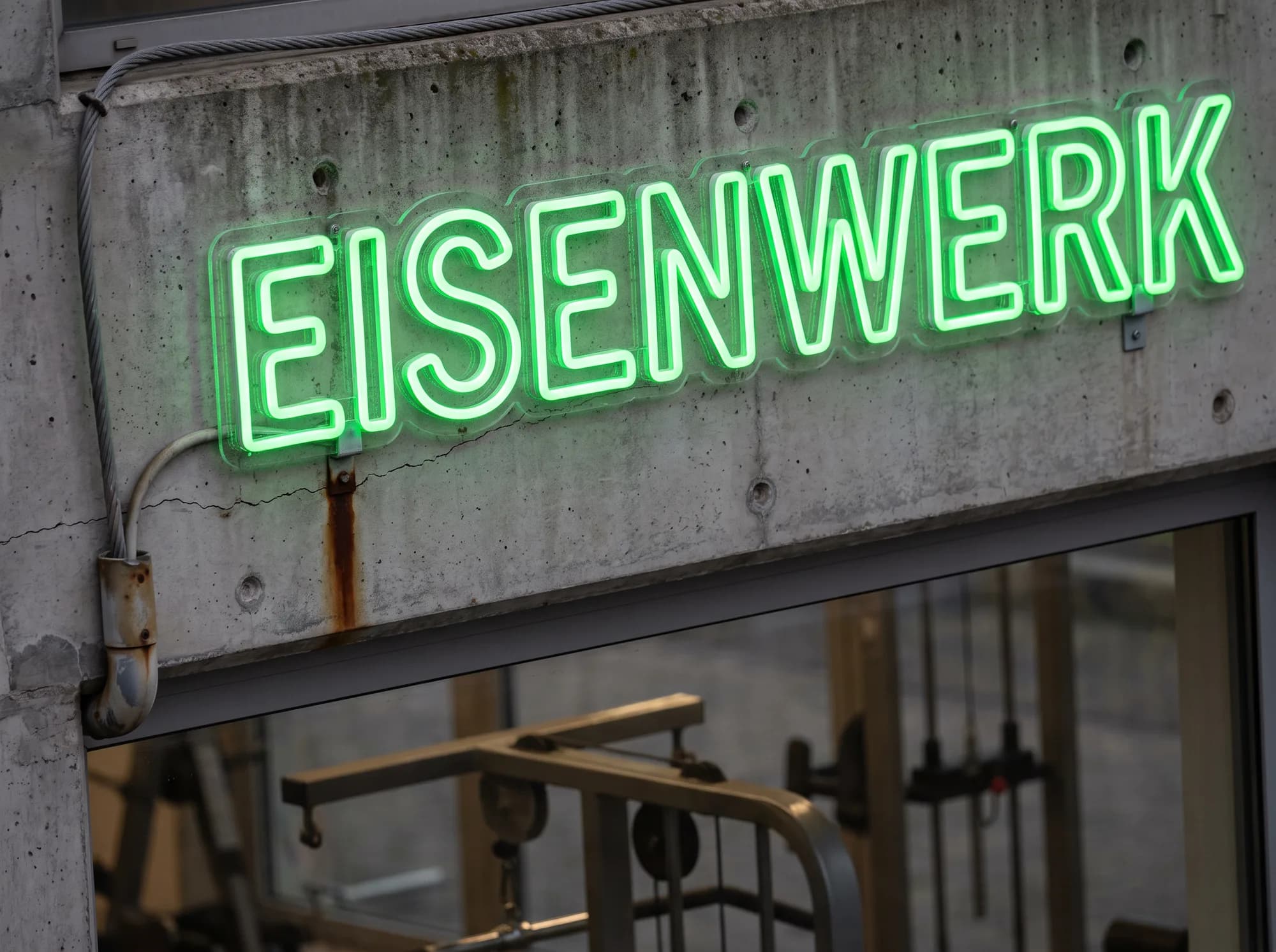 Grüner Neon-Schriftzug in Konturausführung auf dem Betonsturz eines Fitnessstudios