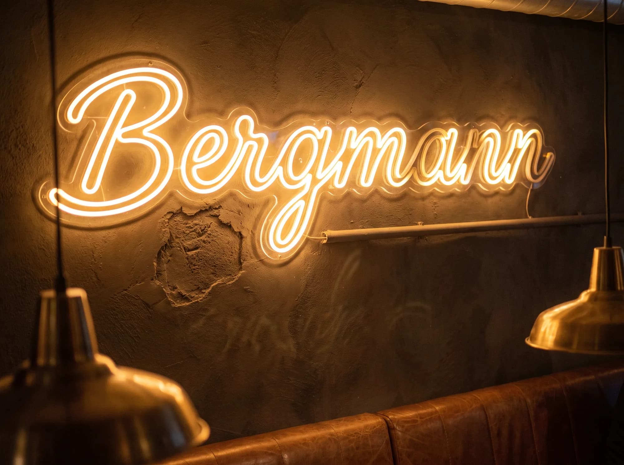Großformatiger bernsteinfarbener Neon-Schriftzug in Schreibschrift an der Rückwand eines Restaurants